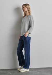Maglione grigio strutturato con maniche a tre quarti, abbinato a jeans diritti blu scuro e sneakers bianche. Look semplice e informale.