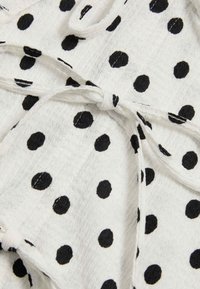 Hvidt stof med en tekstureret overflade, med sorte polkaprikker og en detaljeret taljebinding. Mønsteret er jævnt fordelt over materialet.