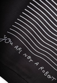 Sudadera negra con rayas horizontales blancas y el texto "no eres un robot" en la parte inferior. Textura suave, dobladillo acanalado.