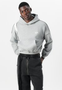Grå cropped hoodie lavet af blødt stof, med et asymmetrisk design og flossede kanter samt en front lomme. Sammen med sorte tapered bukser.