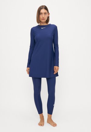 Marineblaues Sportkleid mit langen Ärmeln und Rundhalsausschnitt, kombiniert mit passenden Leggings. Besitzt ein kleines weißes Nike-Logo.