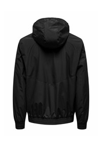 Zwarte windbreakerjas met capuchon, met elastische manchetten en zoom. Gemaakt van soepel, waterafstotend materiaal. Eenvoudig, functioneel ontwerp.