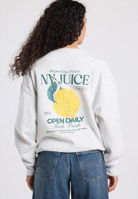 Gray sweatshirt featuring a large colored print on the back with a lemon graphic and text about a juice shop, paired with blue denim.