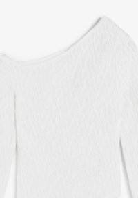 Top blanco fuera de los hombros con tejido texturizado que presenta un patrón ondulado, mangas largas y un escote amplio.
