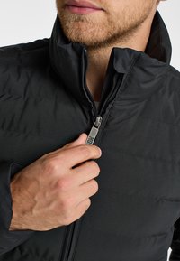 Schwarze isolierte Jacke mit hohem Kragen und Frontreißverschluss, präsentiert eine glatte Textur und ein gestepptes Design auf dem Körper.