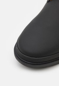 Chaussure en cuir noir avec un bout arrondi, une semelle texturée et une bordure contrastante le long du bord. Finition lisse avec des détails de design minimaux.