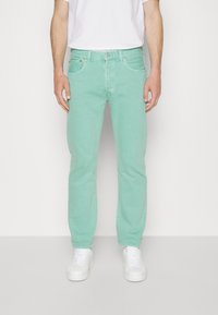 Ljusgröna denimjeans med rak passform, fem fickor och diskreta sömnadsdetaljer, parat med vita sneakers och en enkel vit t-shirt.