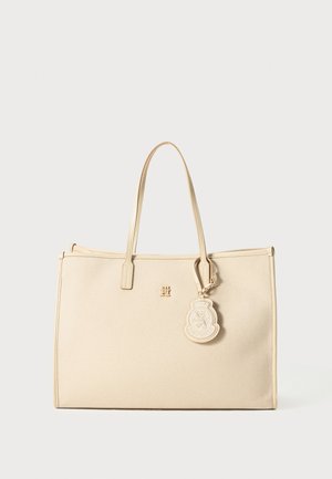Beige tote bag with a textured surface, slim handles, and gold-tone hardware. Features a logo charm attached to one side.