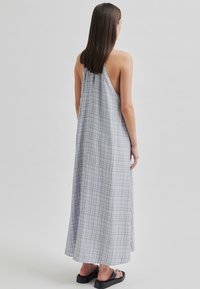 Rochie lungă, fără spate, dintr-un material ușor, de culoare gri deschis, cu un model de rețea format din linii subțiri întunecate, terminată cu o margine fluidă.
