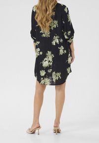 Sort kimono med grønne blomstermønstre, lange ærmer og løs pasform, der har en buet kant og blødt, let stof.