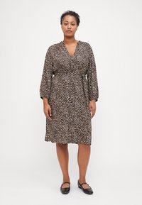 Robe imprimée léopard avec manches longues, design enveloppant, taille cintrée, longueur genoux, fabriquée en tissu doux, présentant un motif marron et noir.