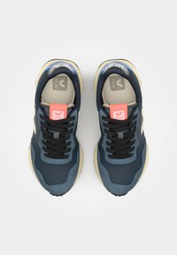 Navy blue athletic shoes with black laces, beige sole, textured upper, and pink accents; features logo on tongue and side.