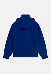 Granatowa kurtka przeciwwiatrowa z kapturem, elastycznymi mankietami i dolnym obszyciem. Posiada logo na kołnierzu oraz gładką, lekką tkaninę.