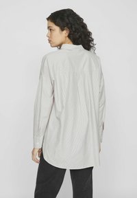 Camisa de manga larga color gris claro con cuello, pliegue en la espalda y puños abotonados. Presenta un sutil patrón de rayas verticales y un ajuste relajado.