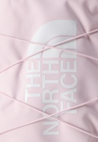 Ροζ ύφασμα με λευκό λογότυπο The North Face, μερικώς καλυμμένο από διασταυρούμενα ροζ ελαστικά κορδόνια.