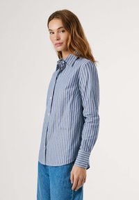 Camicia a maniche lunghe blu e bianca a righe con colletto button-down, dotata di tasca sul petto e orlo leggermente curvo per un fit rilassato.