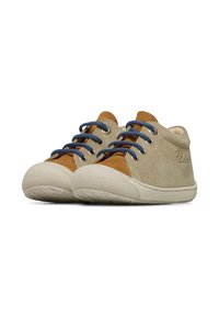 Des chaussures pour enfants en suede beige avec des accents marron, présentant des lacets bleus, une semelle en caoutchouc blanc texturé et un design de bout arrondi.