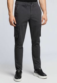 Grå cargobyxor med slim fit, featuring sidofickor, subtil textur och knappstängning, ihop med svarta sneakers.