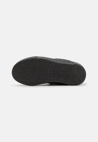 Suela de zapato de goma negra con textura y dibujo en el relieve. Presenta un ligero borde y un logo en relieve cerca del centro.