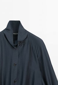 Mörk marinblå jacka med hög krage och knappar, subtil vertikal struktur och långa raglanärmar, märkt Massimo Dutti.