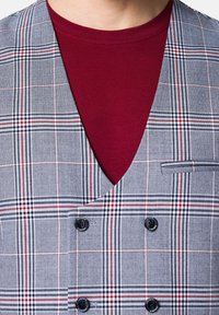 Szara kamizelka w kratę z czerwonymi i granatowymi akcentami, z dekoltem w serek, podwójnym zapięciem na guziki oraz bordową koszulą pod spodem.