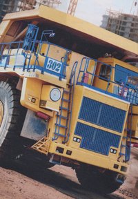 Gul gruvtruck med blå accenter, stora däck, synliga steg och räcken, frontgaller med nät, och numrerad 302. Byggarbetsplats i bakgrunden.