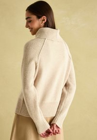 Beeside vahepealne joontega kampsun kõrge ribaga kraega, ribadega mansettide ja lõdva fitiga. Pehme tekstuur, esitades puhta tagapoolse disaini.