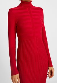Rotes Strickkleid mit langen Ärmeln und hohem Kragen. Verfügt über gerippte Textur und horizontale Streifen im oberen Teil.