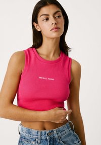 Aansluitende geribbelde crop top in felroze met een ronde hals en de tekst "RED BULL RACING" in het wit op de voorkant. Gecombineerd met hoge spijkerbroekshorts.