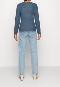 Stickad blå tröja med ribbad mudd och nederkant, i kombination med ljusblå raka jeans och beige blockklackskor.