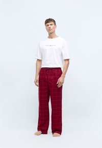Pantalons de pyjama à carreaux rouges avec une taille à cordon, associés à un t-shirt à manches courtes blanc avec un logo au centre.