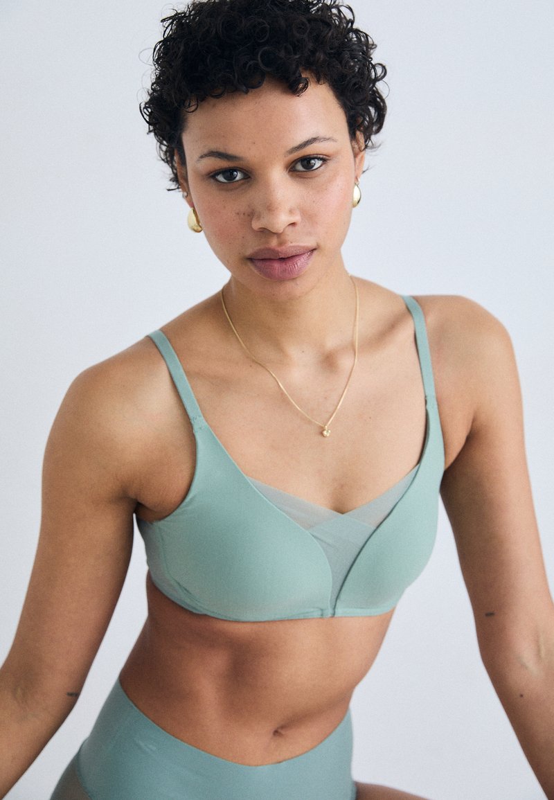Light green seamless bra with adjustable straps and a V-shaped design. Textured mesh accent at the center. Smooth fabric, minimalistic style.