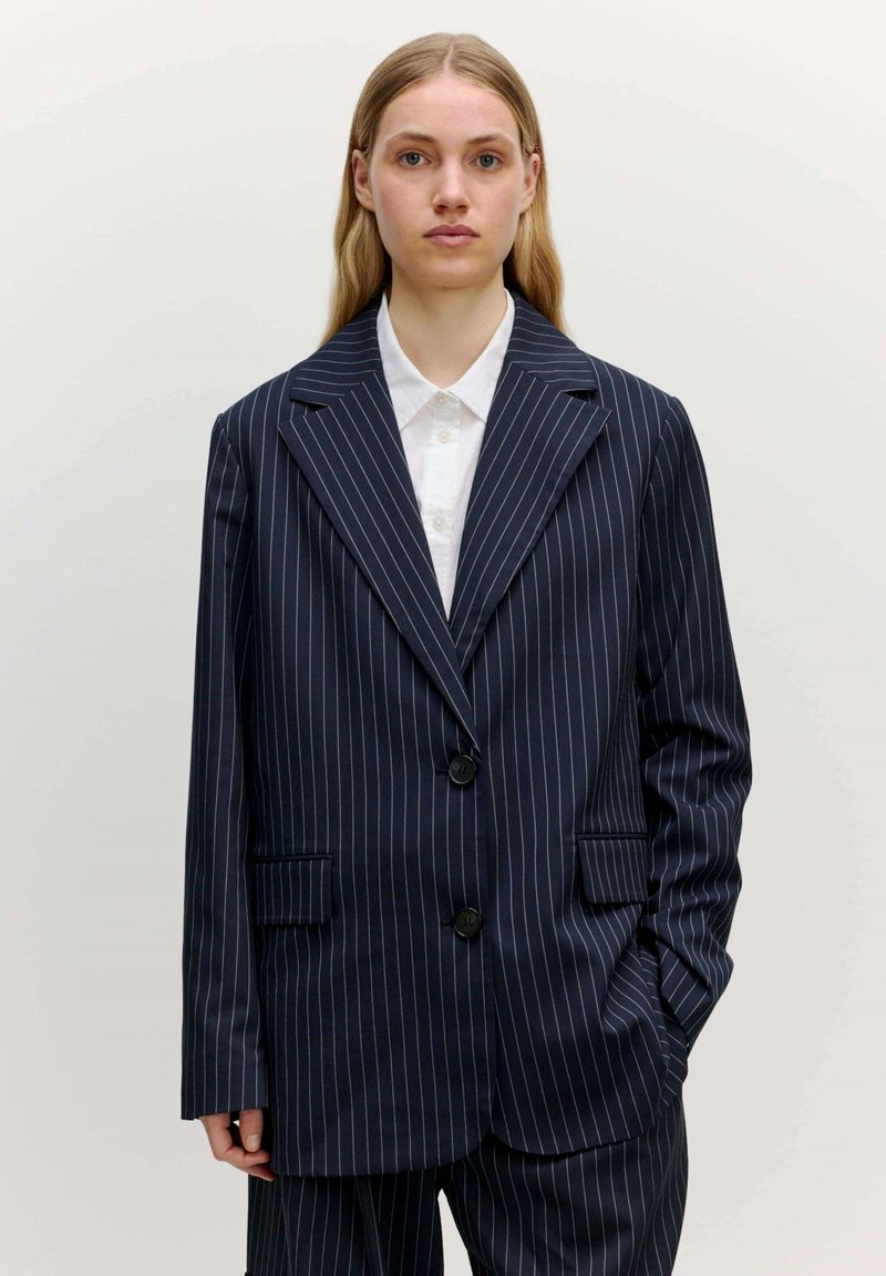 Marineblaues gestreiftes Blazer, strukturierte Form mit geknoteten Revers, zwei Fronttaschen und Zwei-Knopf-Verschluss. Glatte Stofftextur.