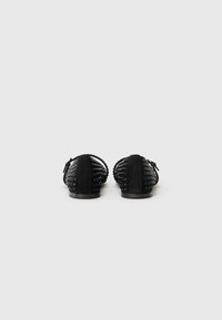Ballerines en daim noir avec des accents de clous décoratifs et un design tissé. Bout rond et semelle plate, avec un petit nœud sur le côté.