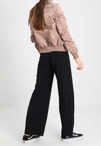 Ljusrosa bomberjacka med ribbade muddar och fåll, kombinerad med svarta vida byxor och svarta sneakers. Slät tyg, avslappnad passform.