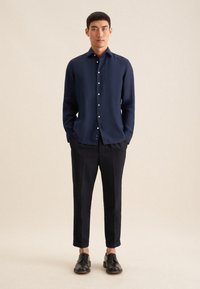 Marineblauwe lange mouw shirt met knopen, gecombineerd met zwarte cropped broeken en zwarte nette schoenen. Gladde textuur, getailleerde pasvorm, minimalistisch ontwerp.