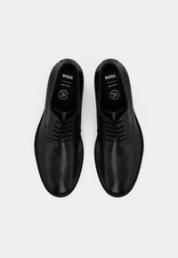 Chaussures en cuir noir à finition lisse, dotées d'un design à lacets et d'un bout arrondi. Semelle flexible avec un détail de couture sur le bord.