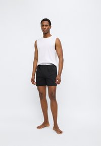 Λευκό αμάνικο μπλουζάκι και μαύρο σορτς με ελαστική μέση. Ομαλό ύφασμα, εφαρμοστή γραμμή και μινιμαλιστικό στυλ.