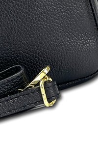 Schwarze Ledertasche mit strukturiertem Pebble-Effekt, ausgestattet mit einem goldenen Metallschloss und einem verstellbaren schwarzen Gurt. Nahaufnahme des Beschlags und der Nähte.