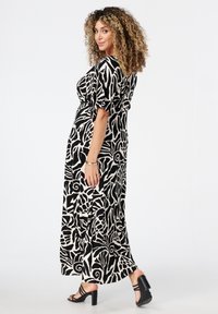 Zwart-wit gedrukte maxi-jurk met abstract patroon, korte puffmouwen, een aangesloten taille en een vloeiende rok. Draagt met zwarte sandalen met bandjes.