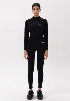 Zwart sportoutfit met een lang mouw, rits-top en hoge taille legging. Soepele textuur, minimalistische ontwerp, met merkelementen.