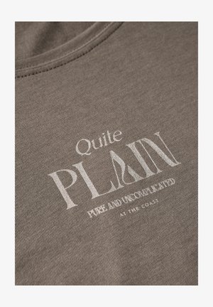 Grå bomullströja med texturerad tyg, rund halsringning och vit tryckt text: "Ganska ENKEL REN OCH OKOMPLOKERAD VID KUSTEN."