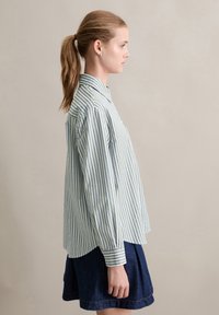 Camicia a righe verde e bianca, con colletto, maniche lunghe, orlo curvo e vestibilità comoda. Abbinata a una gonna di jeans.