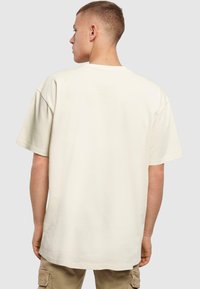 Beige bomulls t-skjorte med kort erm og avslappet passform, med en rund halslinning. Glatt tekstur, minimal merkevare, og en litt forlenget bak.
