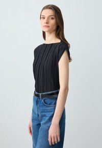 Blusa nera plissettata con scollo a quadrato e maniche corte, abbinata a jeans in denim azzurro a vita alta e una cintura nera.