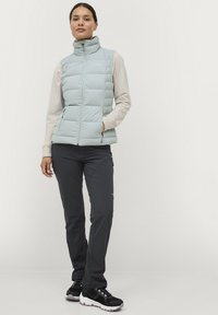 Lichtblauwe puffervest met hoge kraag, horizontaal gestikte ontwerp, zijzakken, gedragen over een licht lange mouw top en donkere broek.