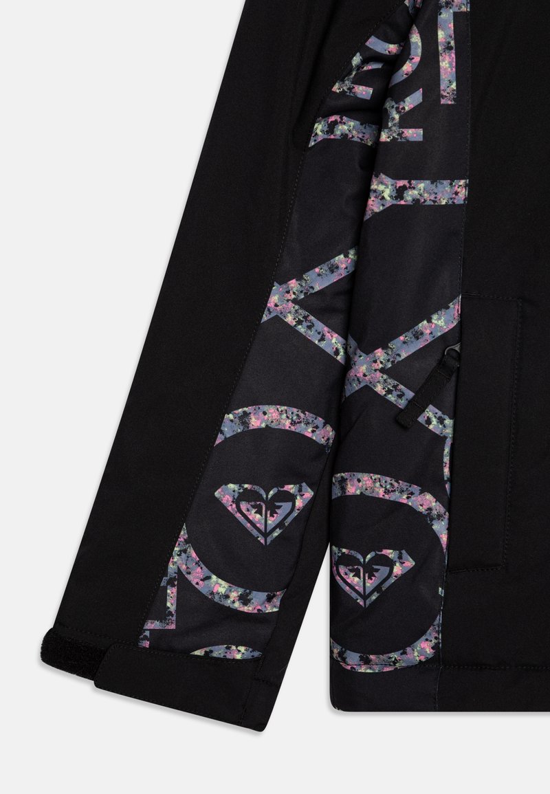 Chaqueta negra con un patrón floral en el forro interior, con logotipos y detalles en rosa, azul y púrpura. Se aprecian detalles del zipper y de la costura.