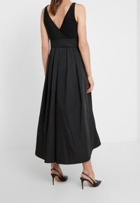 Czarna maxi sukienka z dopasowanym gorsetem, plecami w kształcie litery V i plisowanym dołem. Wykonana z gładkiego materiału. Noszona z czarnymi szpilkami.