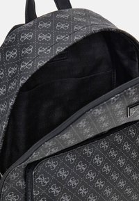 Mochila negra con tela de diseño gris que presenta el logo "GUESS". El interior está forrado con un material negro suave e incluye un bolsillo.