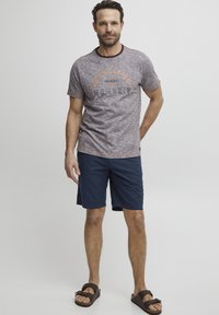 Kortermet, melert grå t-skjorte med trykt design; kombinert med marineblå shorts; sandaler med brune stropper. Hengiven, avslappet passform.